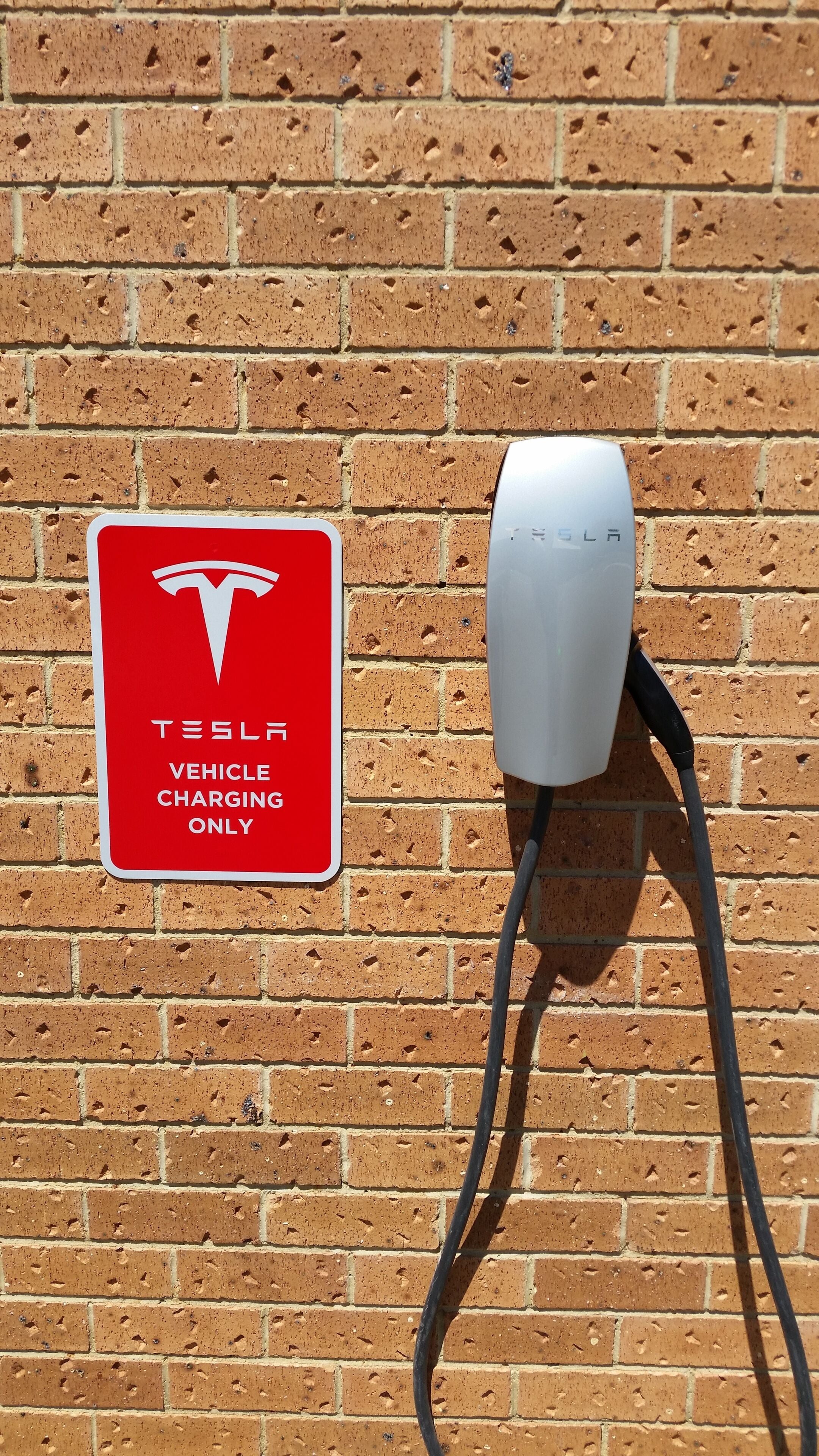A brick wall with a Tesla vehicle charging station and a sign indicating it is for Tesla vehicles only.