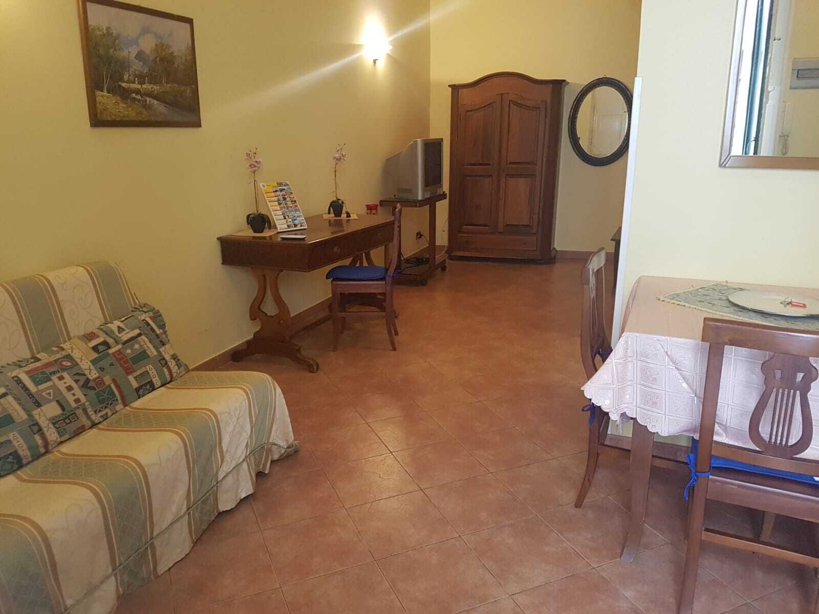 A living room with a sofa, a wooden table with a chair, a TV, and a wardrobe.