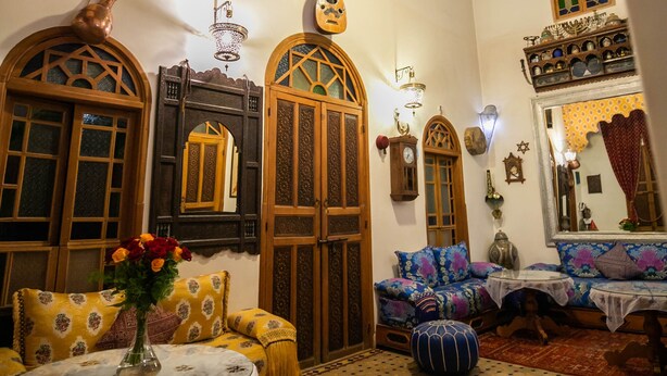A traditional interior with arched wooden doors, a round table with a vase, and patterned cushions. - Riad Les Idrissides (Fes)