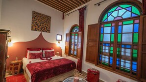 A room with a large bed, a wooden ceiling, a stained glass window, and a tiled floor. - Riad Les Idrissides (Fes)