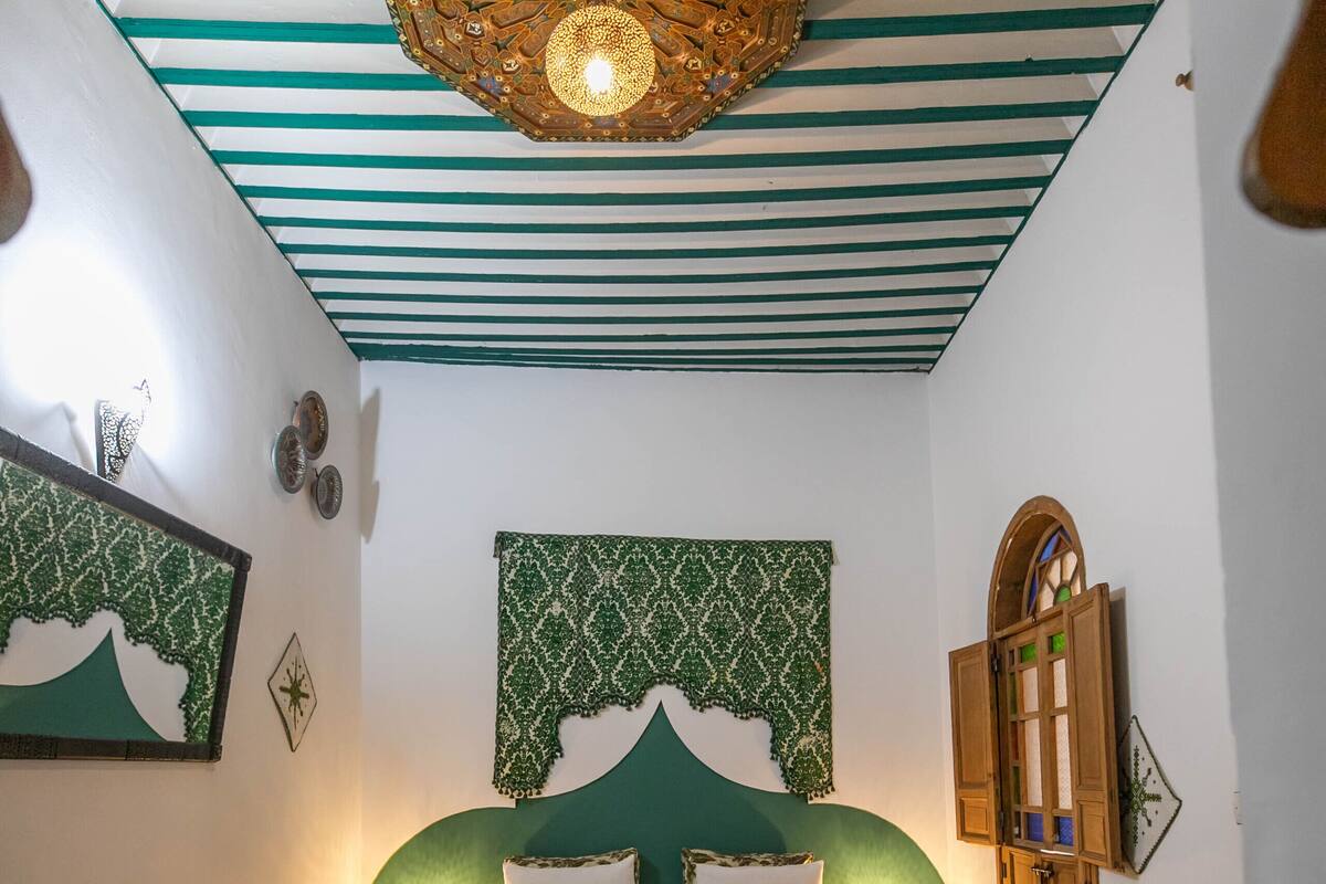 A bedroom with a bed, a round table, a decorative ceiling light, and a patterned wall hanging.