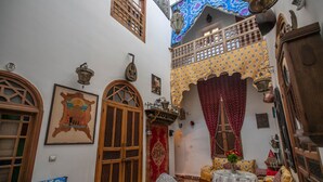 A traditional Moroccan interior with a high ceiling, wooden doors, patterned textiles, and a small dining area. - Riad Les Idrissides (Fes)
