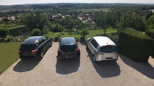 Tres coches aparcados en un camino de grava, con vistas a una zona residencial y vegetación al fondo.
