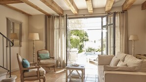 A spacious living room with a high ceiling, wooden beams, a sofa, a chair, a coffee table, and a view through a glass door to an outdoor area. - Château Les Carrasses (Quarante)