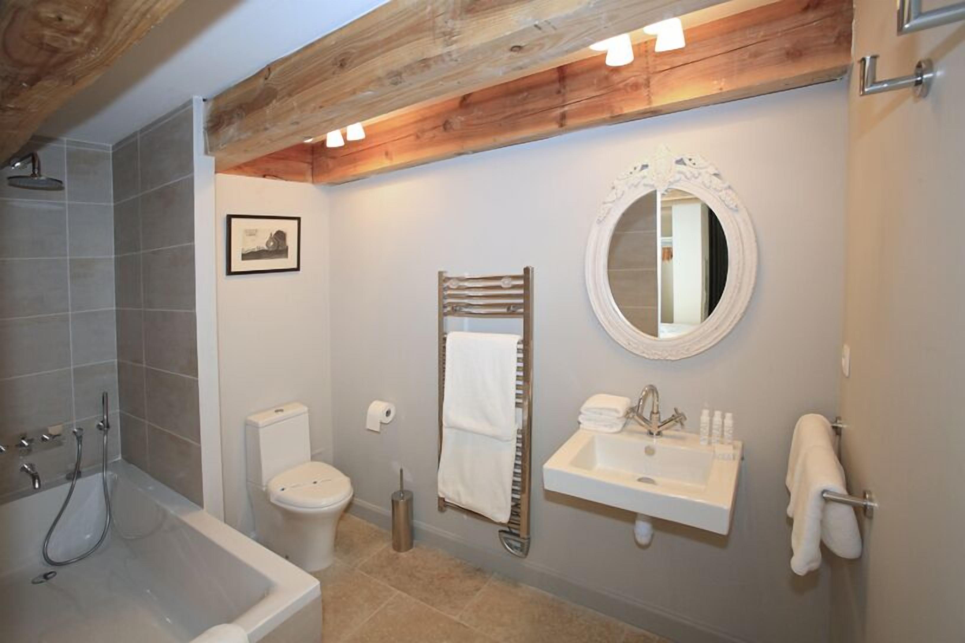 Un baño con bañera, inodoro, lavamanos y una viga de techo de madera.