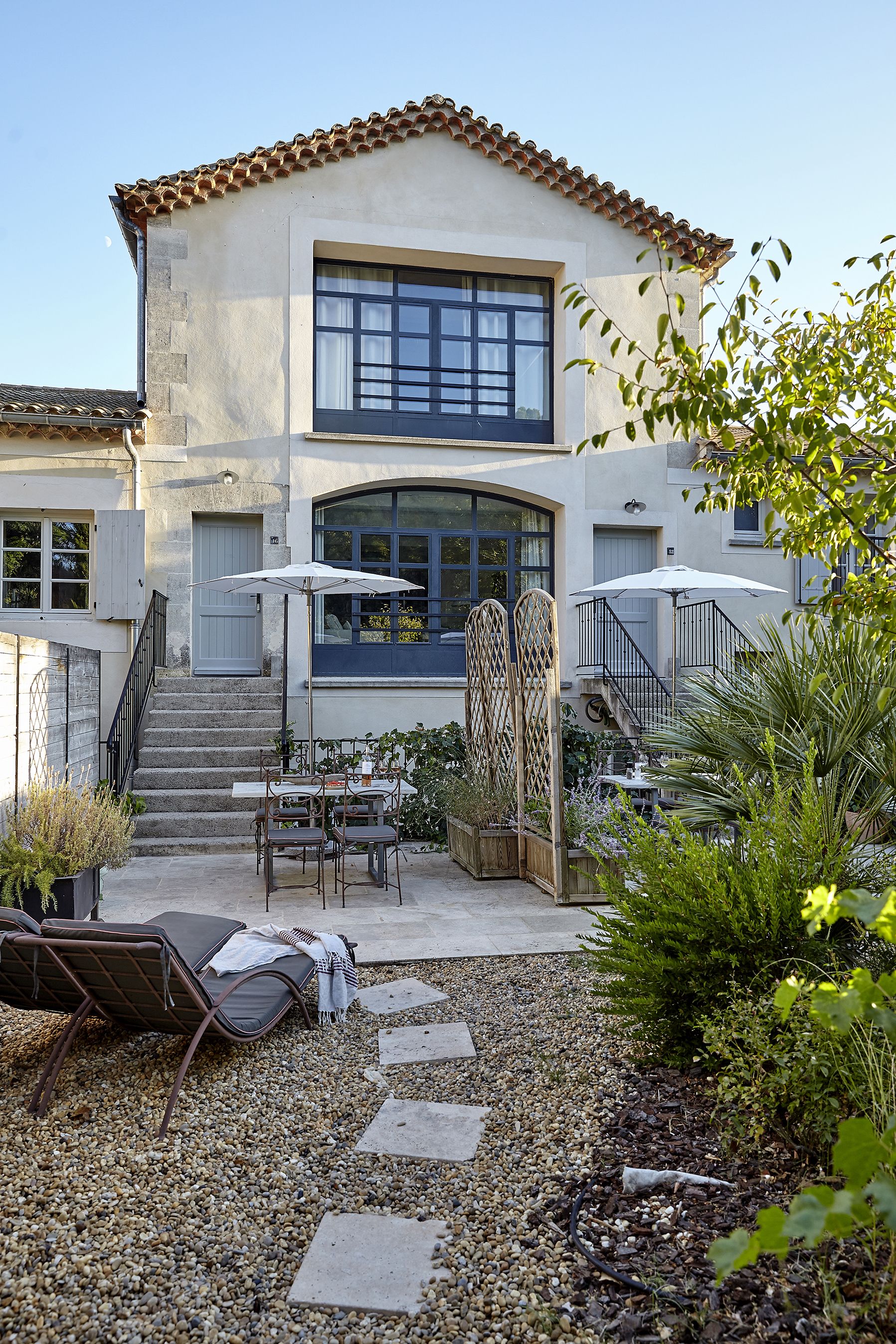 A two-story house with a patio area featuring outdoor furniture, a staircase, and a garden.