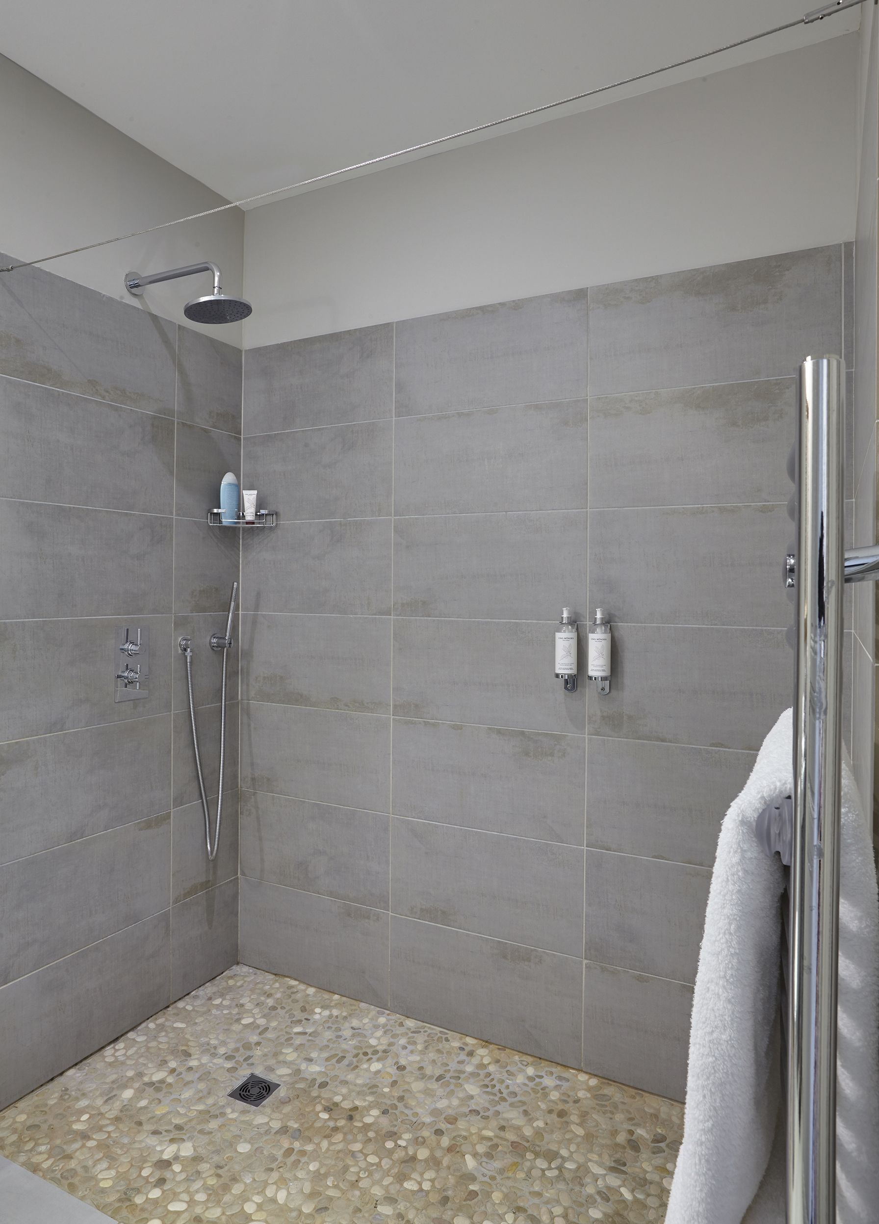 Un moderno espacio de ducha con puerta de vidrio, cabezal de ducha manual y llave de pared.