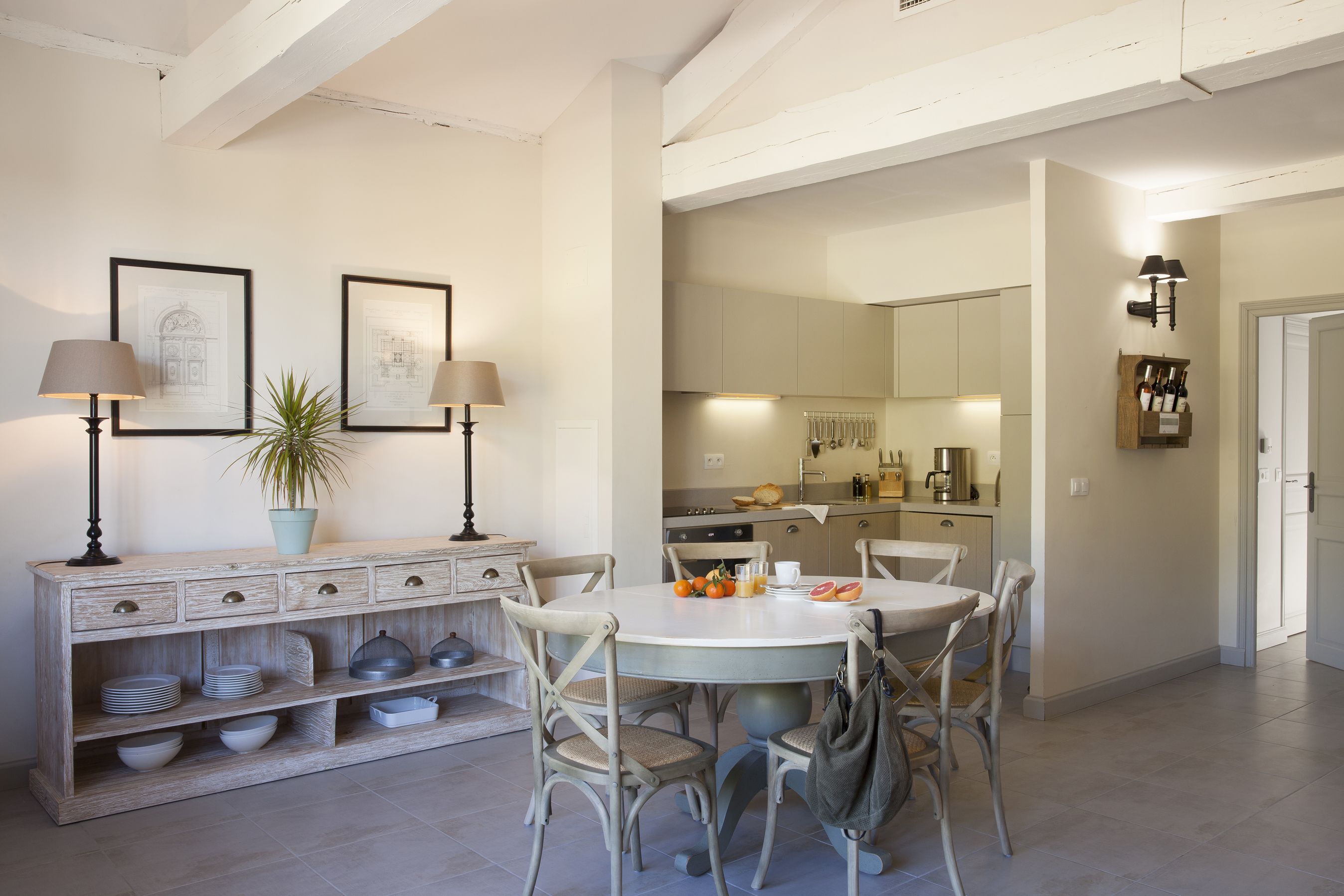 A dining area with a round table, chairs, and a buffet with dishes and a plant.