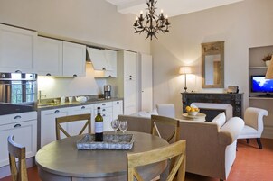 Una cocina moderna con armarios blancos, una mesa de comedor con sillas, una araña y una chimenea.