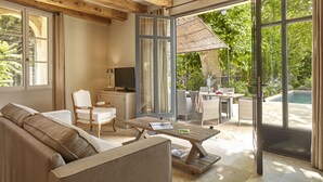 A modern living room with a sofa, coffee table, and TV. It features large windows and a view of a pool and greenery. - Château Les Carrasses (Quarante)