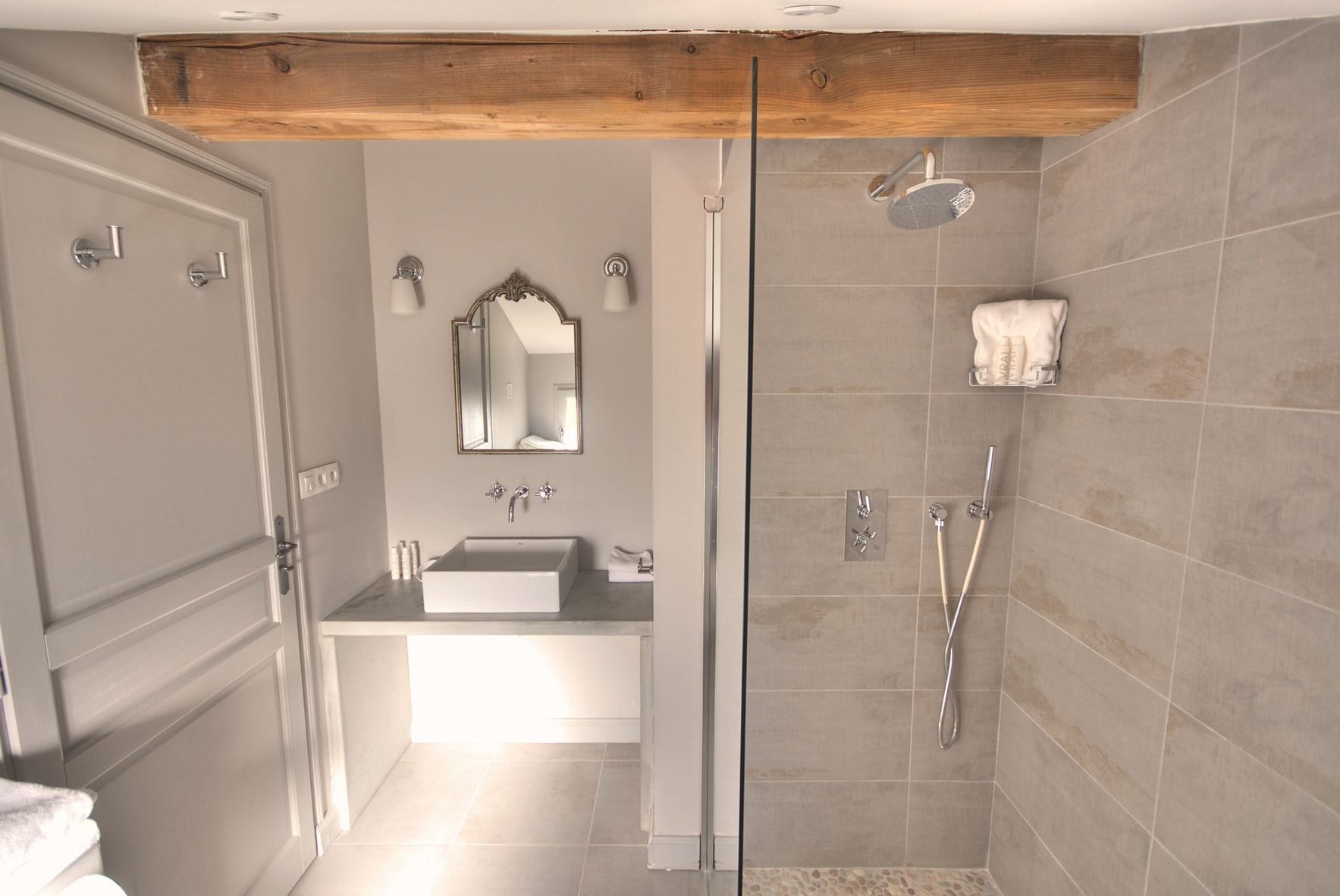 Een moderne badkamer met een glazen douchecabine, een wastafelmeubel met een grote spiegel en een houten balk in het plafond.