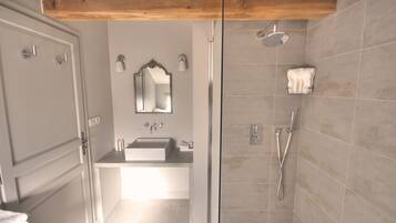 Een moderne badkamer met een glazen douchecabine, een wastafelmeubel met een grote spiegel en een houten balk in het plafond.