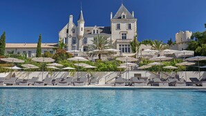 A large, castle-like hotel with a swimming pool, sun loungers, and umbrellas. - Château Les Carrasses (Quarante)
