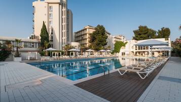 A swimming pool with lounge chairs and umbrellas, surrounded by buildings.
