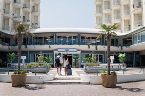 A hotel entrance with a curved facade, multiple balconies, and potted plants.