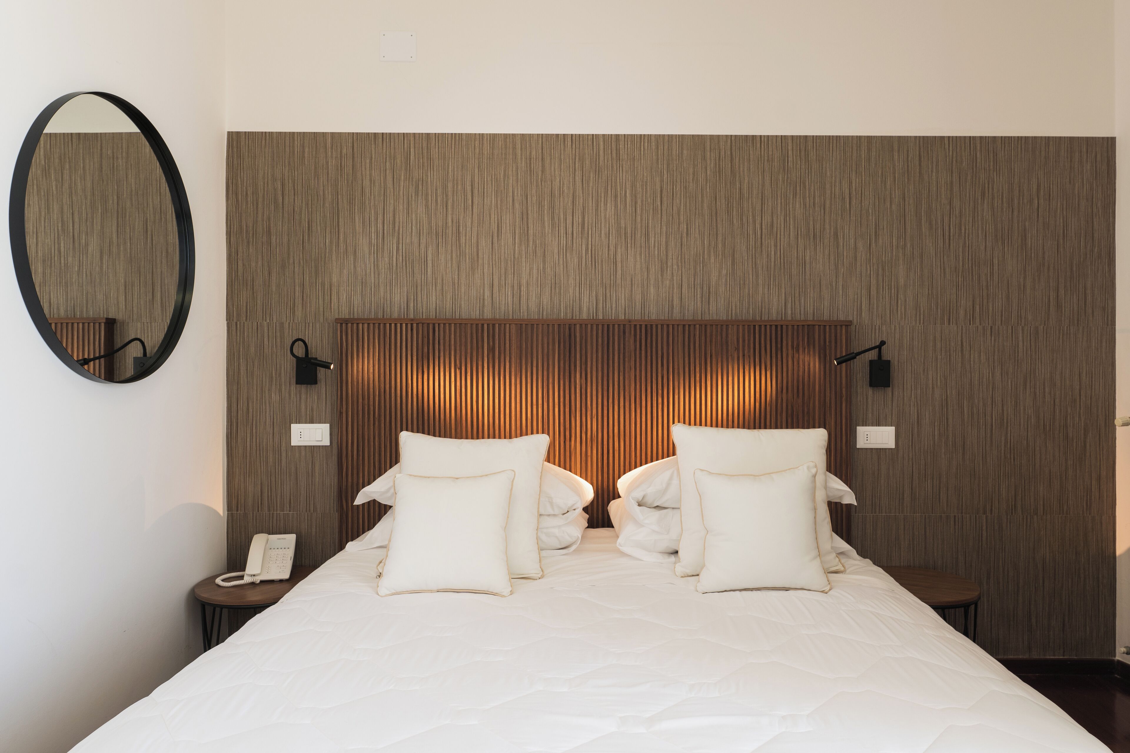 Una habitación de hotel con una cama grande, dos mesitas de noche, un teléfono en la pared y un espejo.