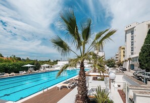 A swimming pool with lounge chairs, a palm tree, and a cityscape in the background.
