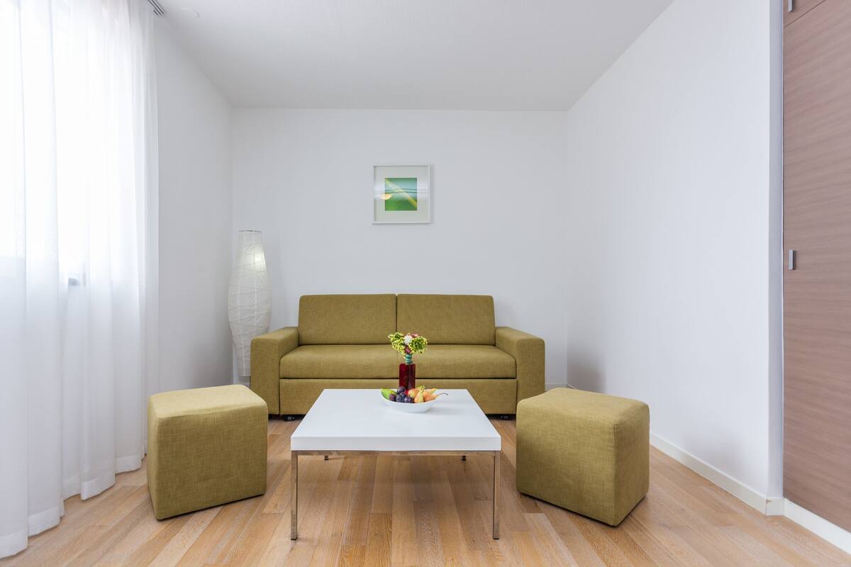 A modern living room with a white coffee table, two green ottomans, a sofa, and a vase with flowers.