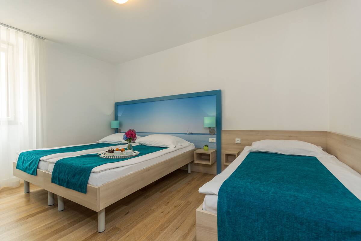 A hotel room with two single beds, a wooden headboard, a nightstand, and a window with curtains.