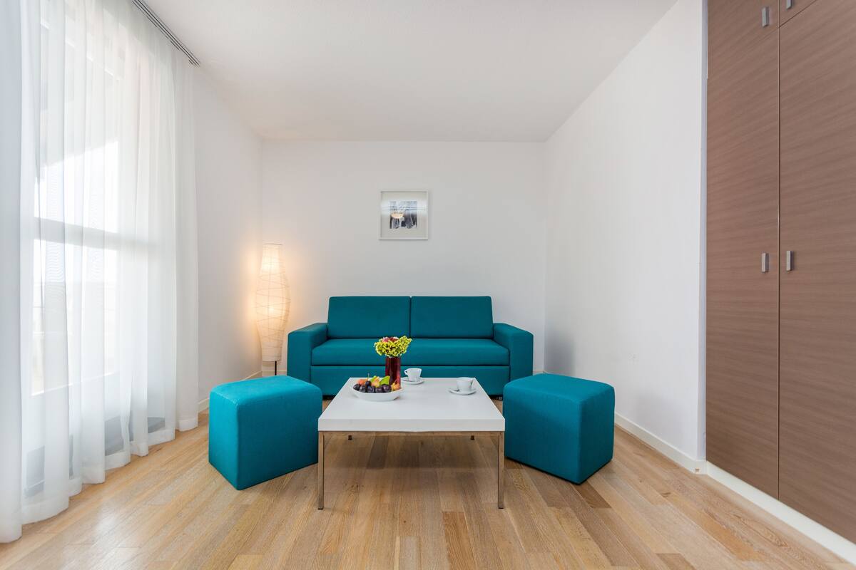 A modern living room with a teal sofa, a white coffee table, and a wooden wardrobe.
