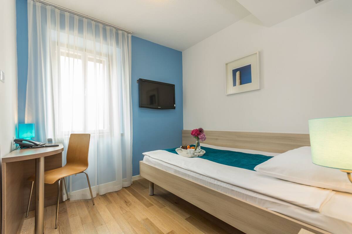 A hotel room with a bed, a desk, a chair, a TV, and a window with curtains.