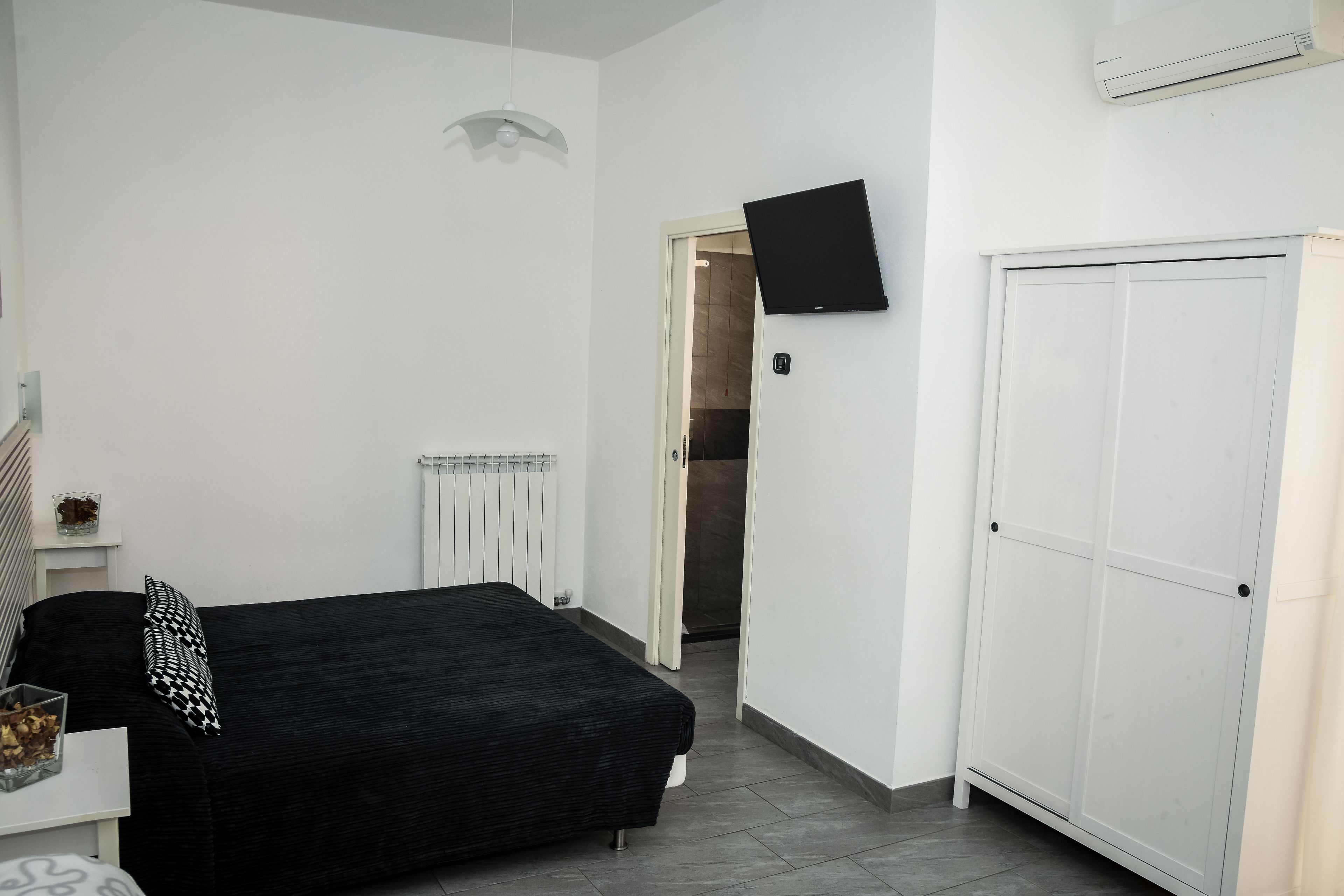 A bedroom with a black sofa, a white wardrobe, a flat-screen TV, and a radiator.