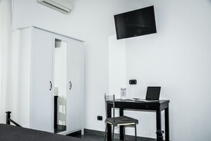Una habitación con un armario blanco, un escritorio con una computadora portátil y un televisor de pantalla plana montado en la pared.