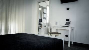 Een hotelkamer met een bed, een bureau met een laptop, een stoel en een aan de muur bevestigde televisie.