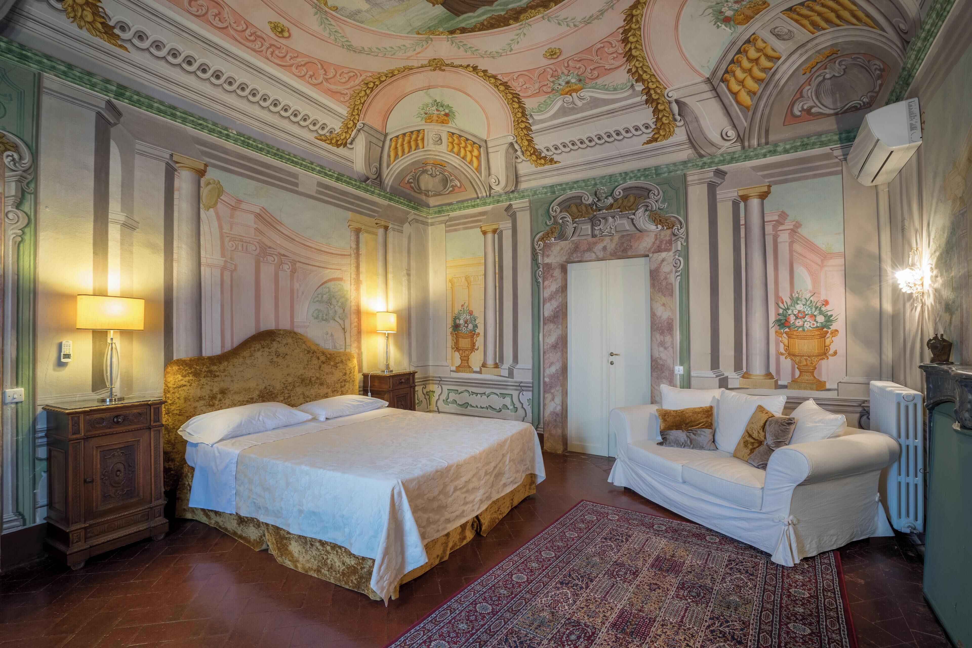 A luxurious bedroom with a large bed, a sofa, and ornate ceiling decorations.