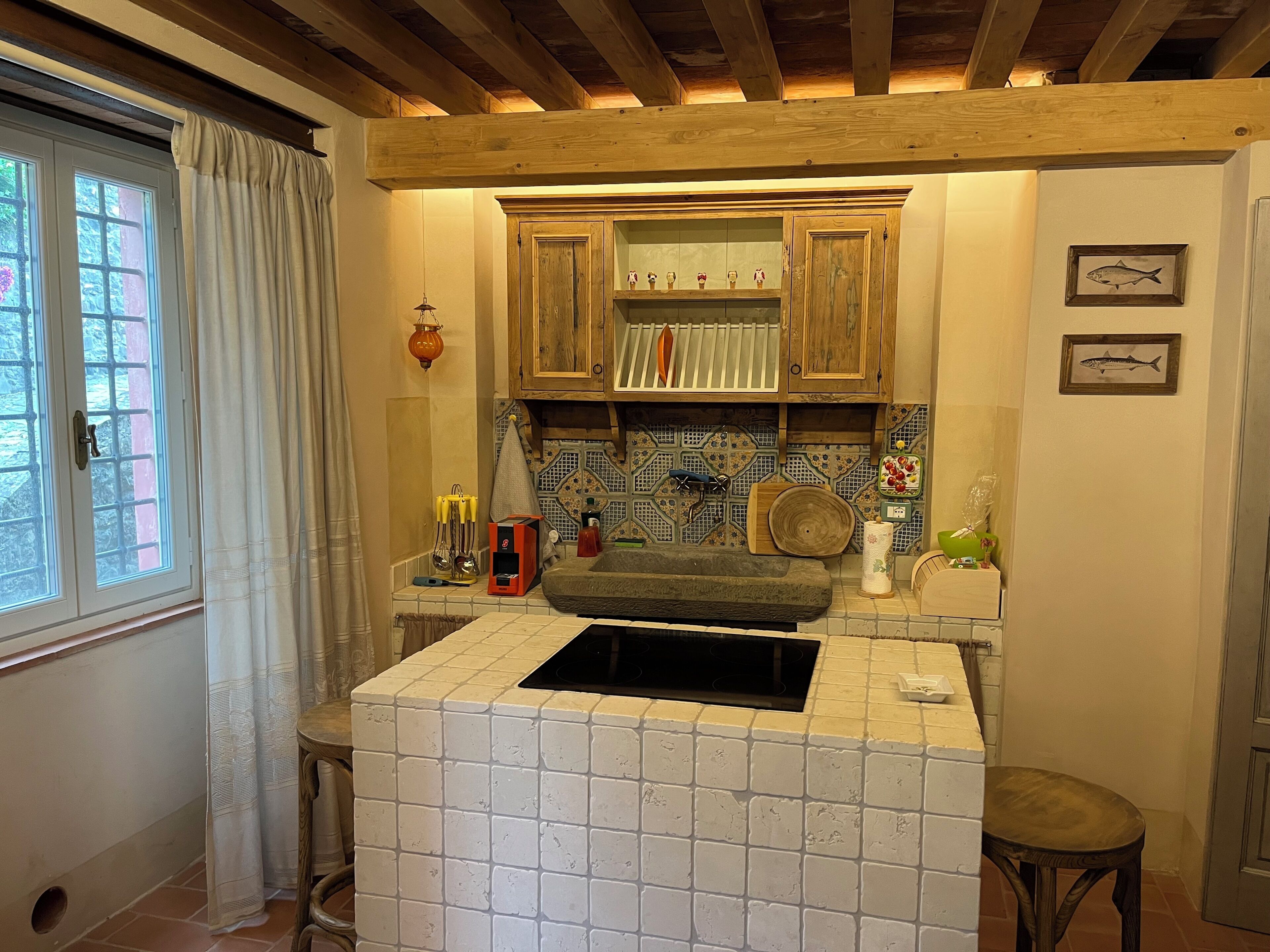 A kitchen with a built-in stove, wooden cabinets, a tiled backsplash, and a window with curtains.