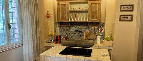 A kitchen with a built-in stove, wooden cabinets, a tiled backsplash, and a window with curtains.