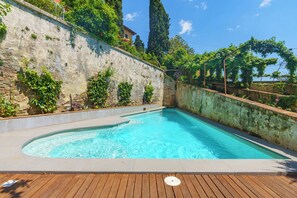 Una piscina con cubierta de madera, rodeada por un muro de piedra y abundante vegetación.