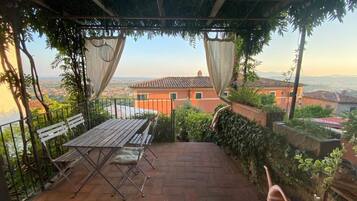 A covered patio with a table and chairs, a view of the cityscape, and a pergola with vines.