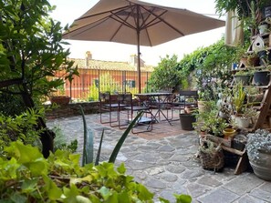 Un patio al aire libre con suelo de piedra, una mesa, sillas, una sombrilla y plantas en macetas.