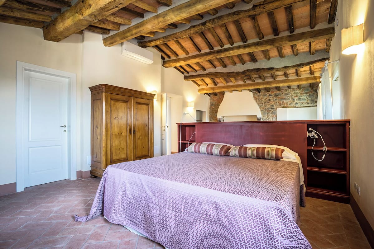 Un dormitorio con techo de madera, cama con ropa de cama estampada, armario y zona de ducha.