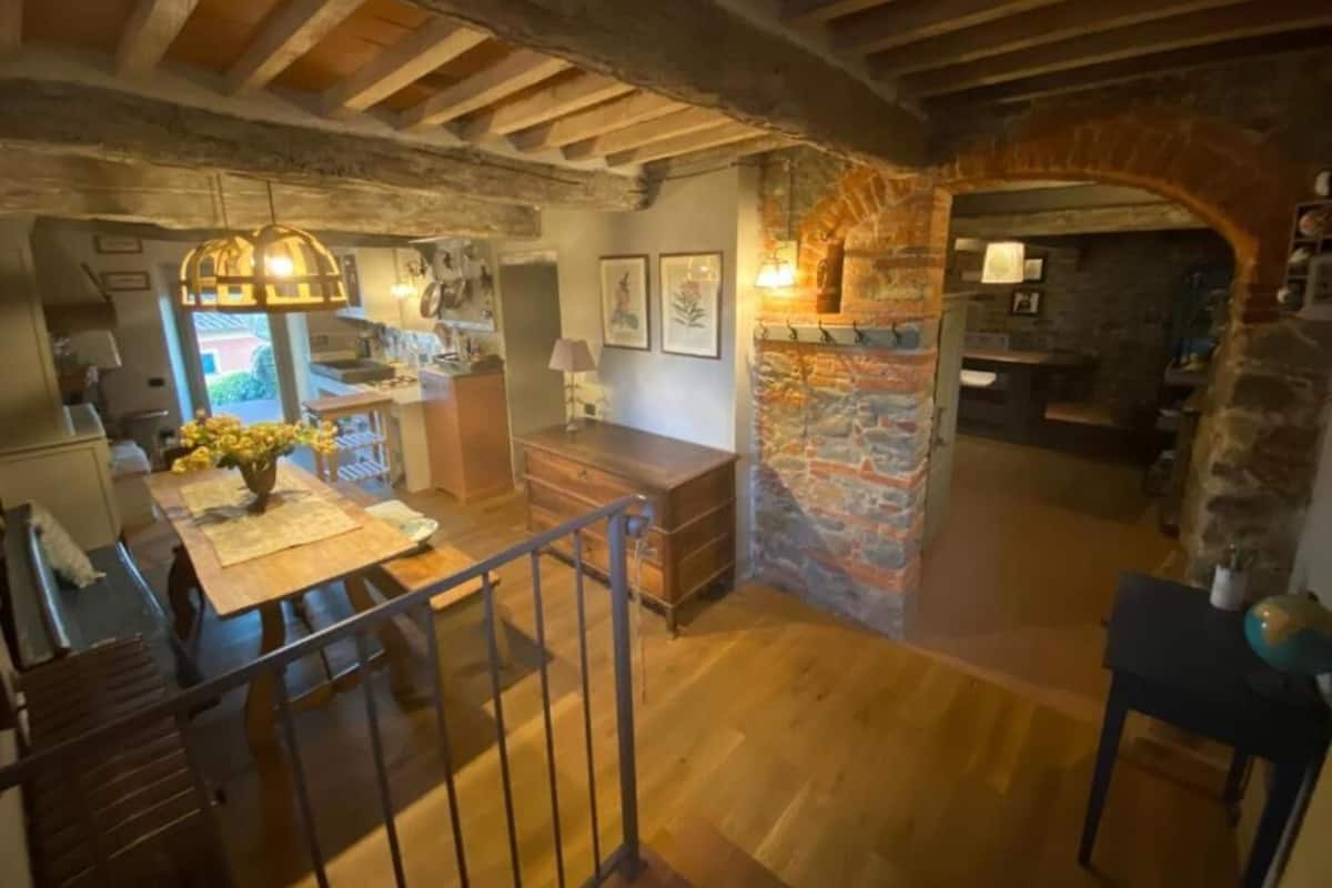 Un interior rústico con vigas de madera a la vista, una pared de piedra y una mesa de comedor de madera con sillas.