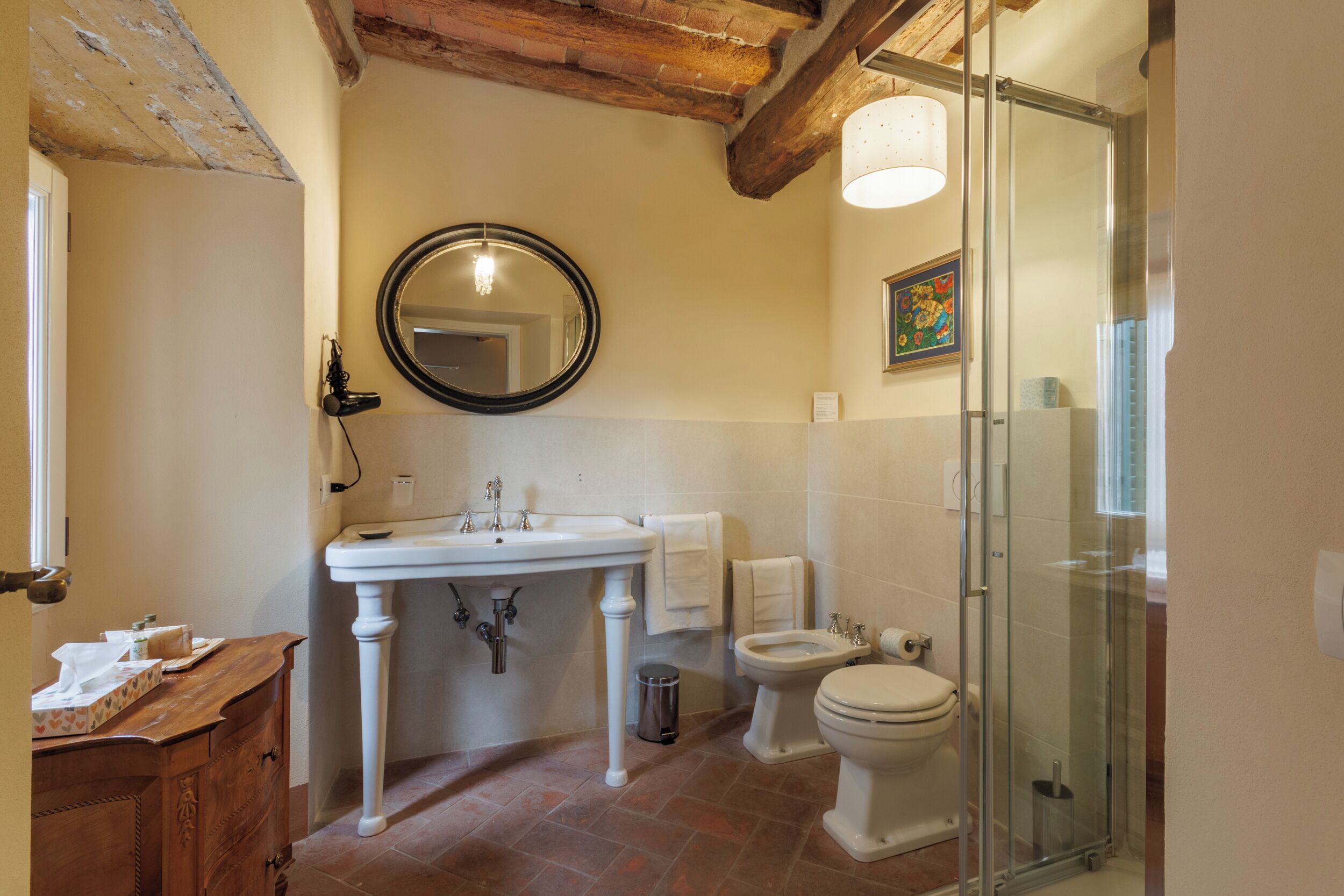 Ein Badezimmer mit einem Standwaschbecken, einem runden Spiegel, einer Toilette und einer Duschkabine.