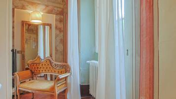 A room with a wooden chair, a mirror, and a radiator.