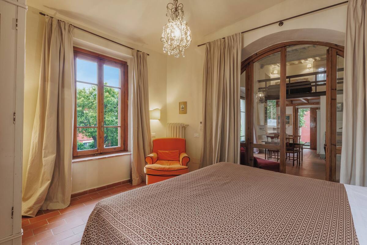 Un dormitorio con una cama grande, una silla, un candelabro y vistas al exterior a través de una ventana.