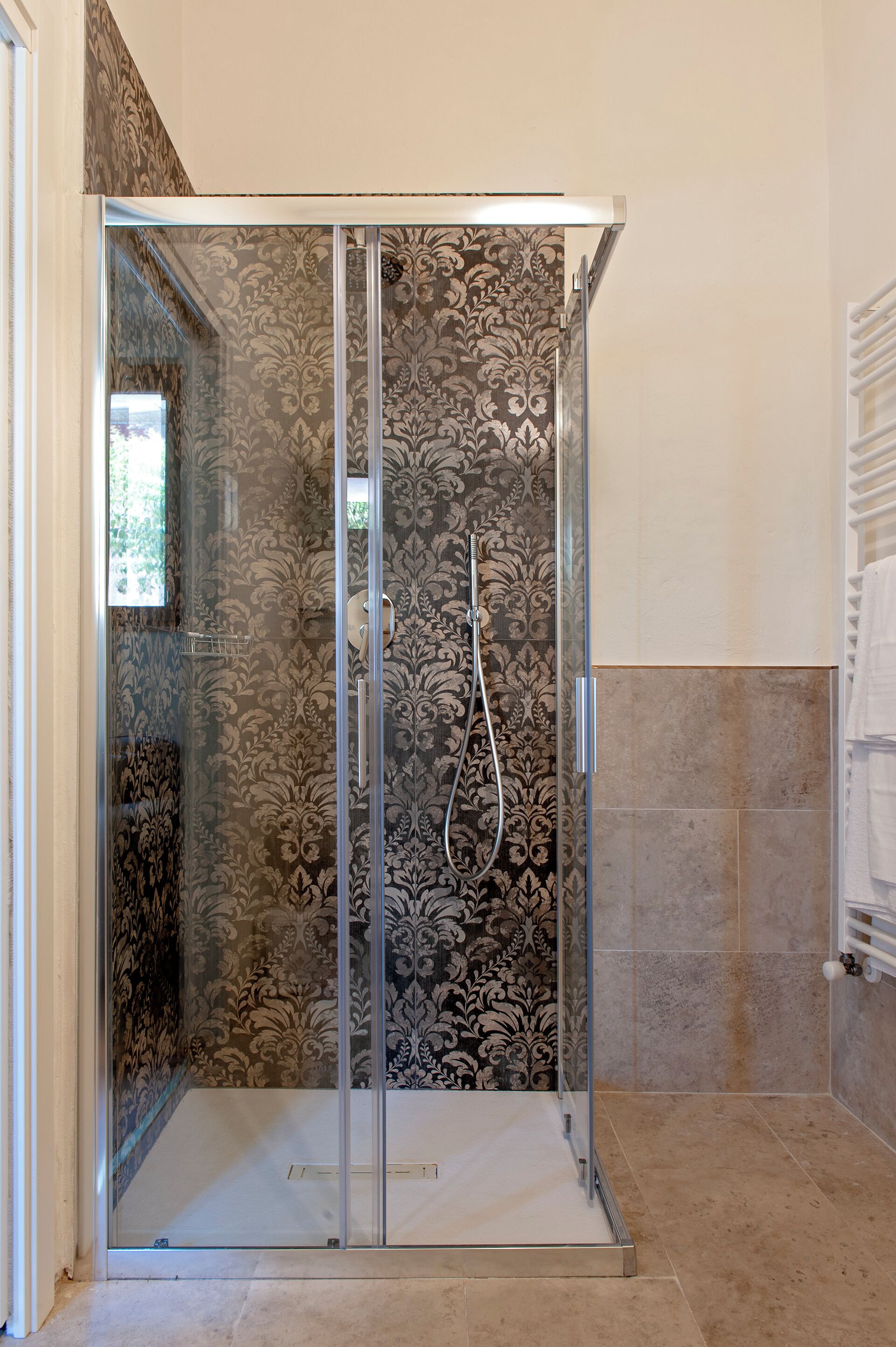 Une douche fermée par des parois de verre, avec un mur décoré et un sol carrelé.