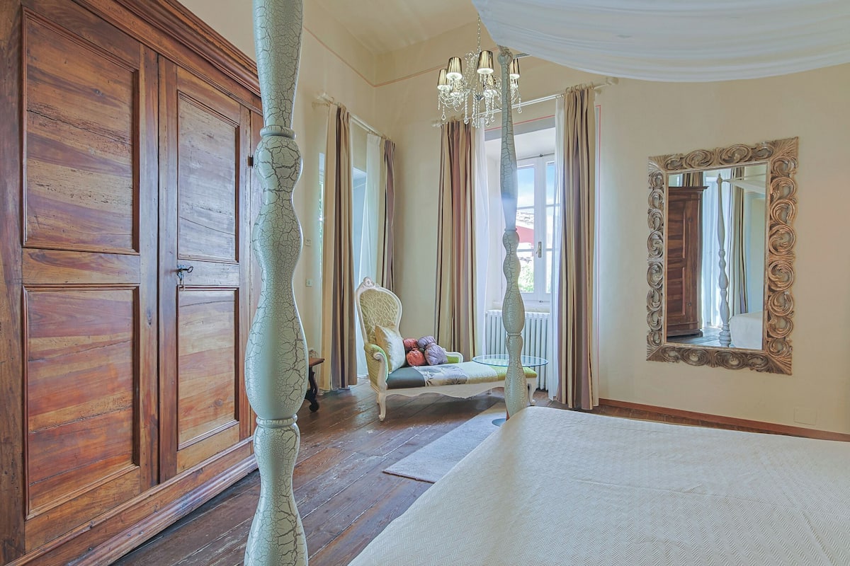Una habitación amplia con un gran armario de madera, un sillón cómodo con cojines, una cama blanca y un espejo decorativo.