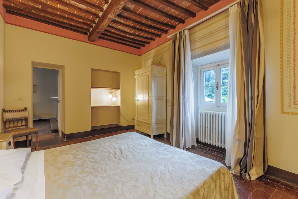 Un dormitorio con una cama grande, un banco de madera, un armario y una ventana con cortinas.