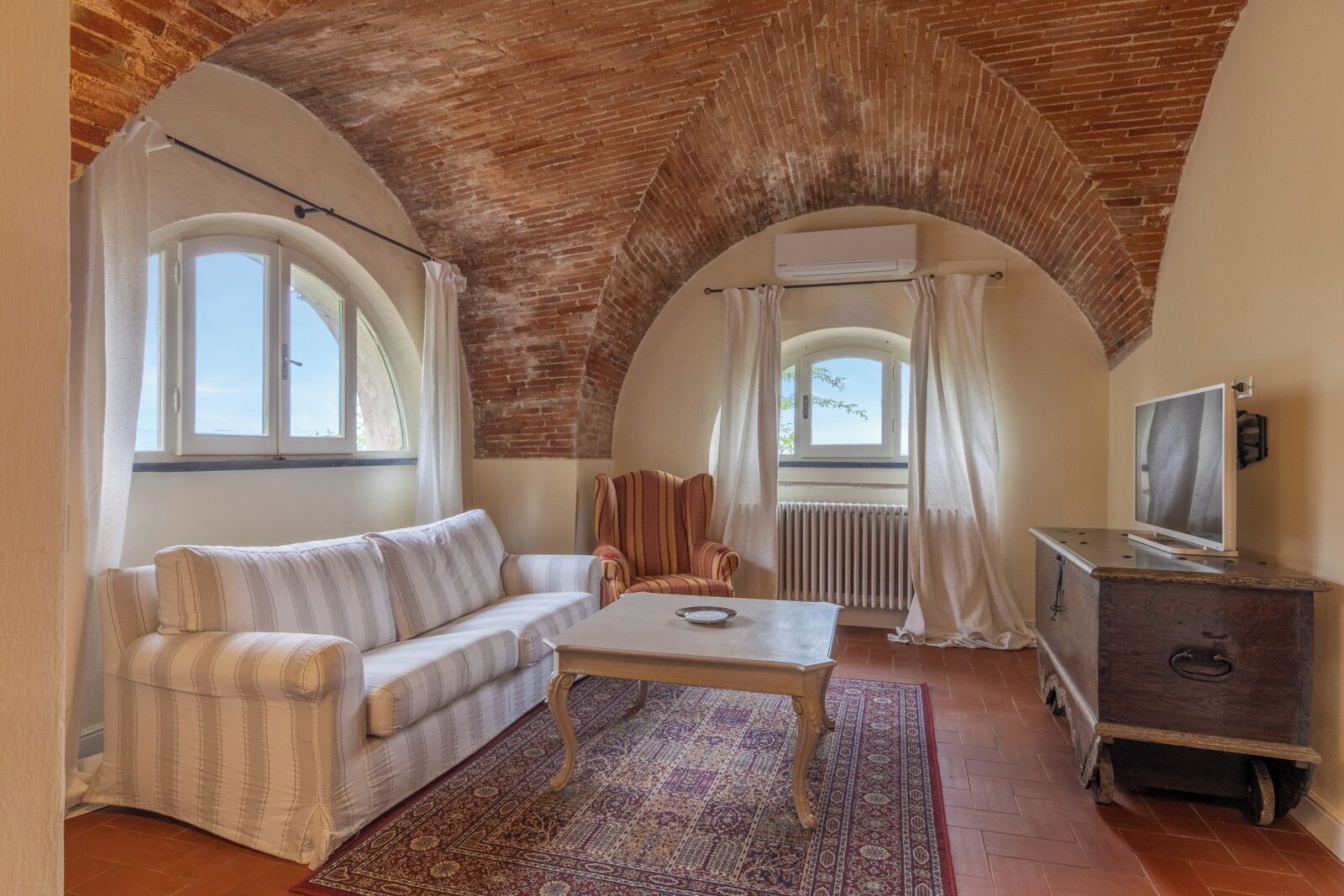 Ein gemütliches Zimmer mit einer hohen, gewölbten Decke, einem Sofa, einem Couchtisch, einem Fernseher auf einer Holzkommode und einem gemusterten Teppich.