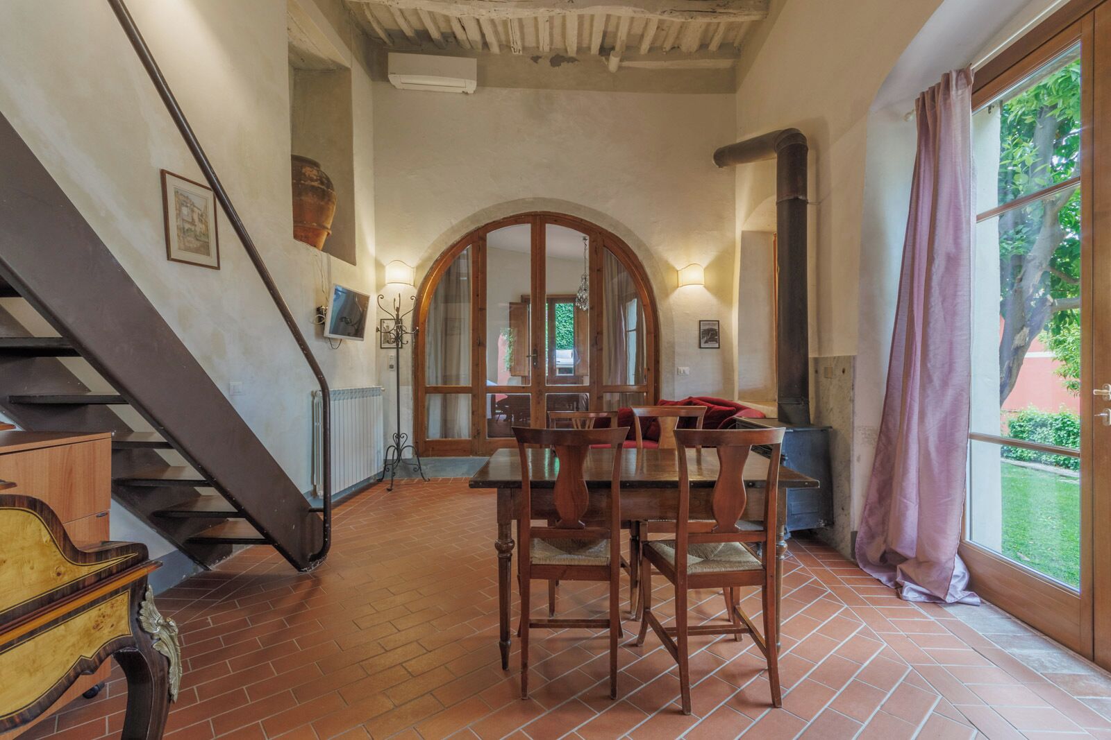A dining area with a wooden table and chairs, a staircase, and a view of the outdoors.