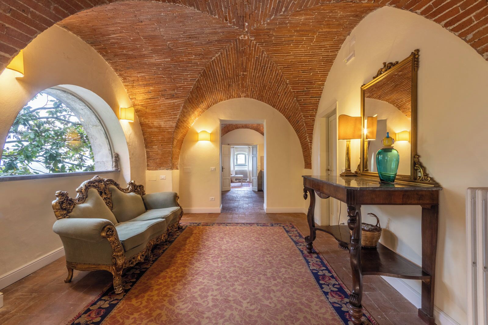 A hallway with a brick ceiling, a sofa, a console table with a mirror, and a patterned carpet.