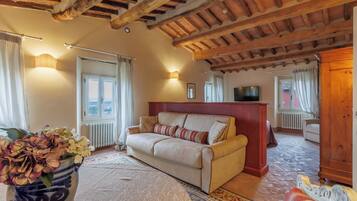 A cozy living room with a sofa, a wooden ceiling, a radiator, and a TV.