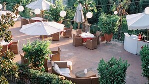 Un patio al aire libre con mobiliario de mimbre, sombrillas y plantas en macetas.