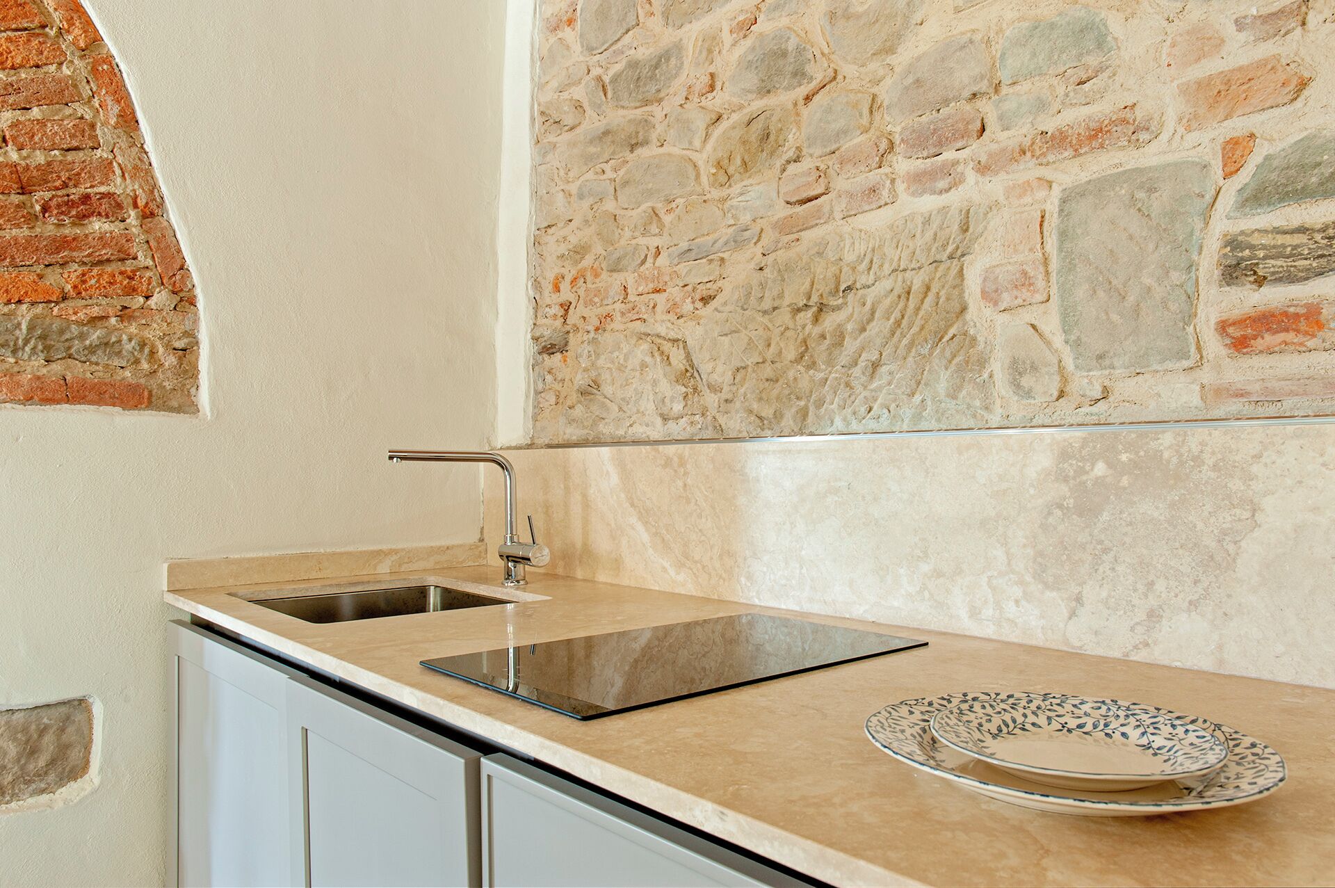 A kitchen with a built-in sink, a countertop, and a stone wall.