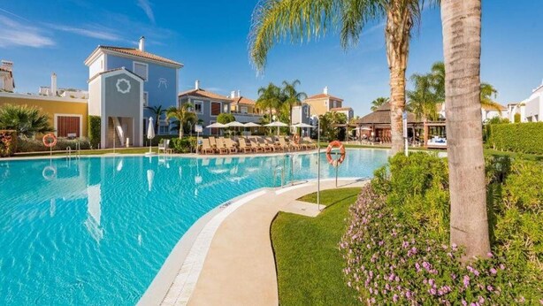 A swimming pool with lounge chairs, palm trees, and a clear blue sky. -  Apartamentos Cortijo del Mar Resort (Estepona)