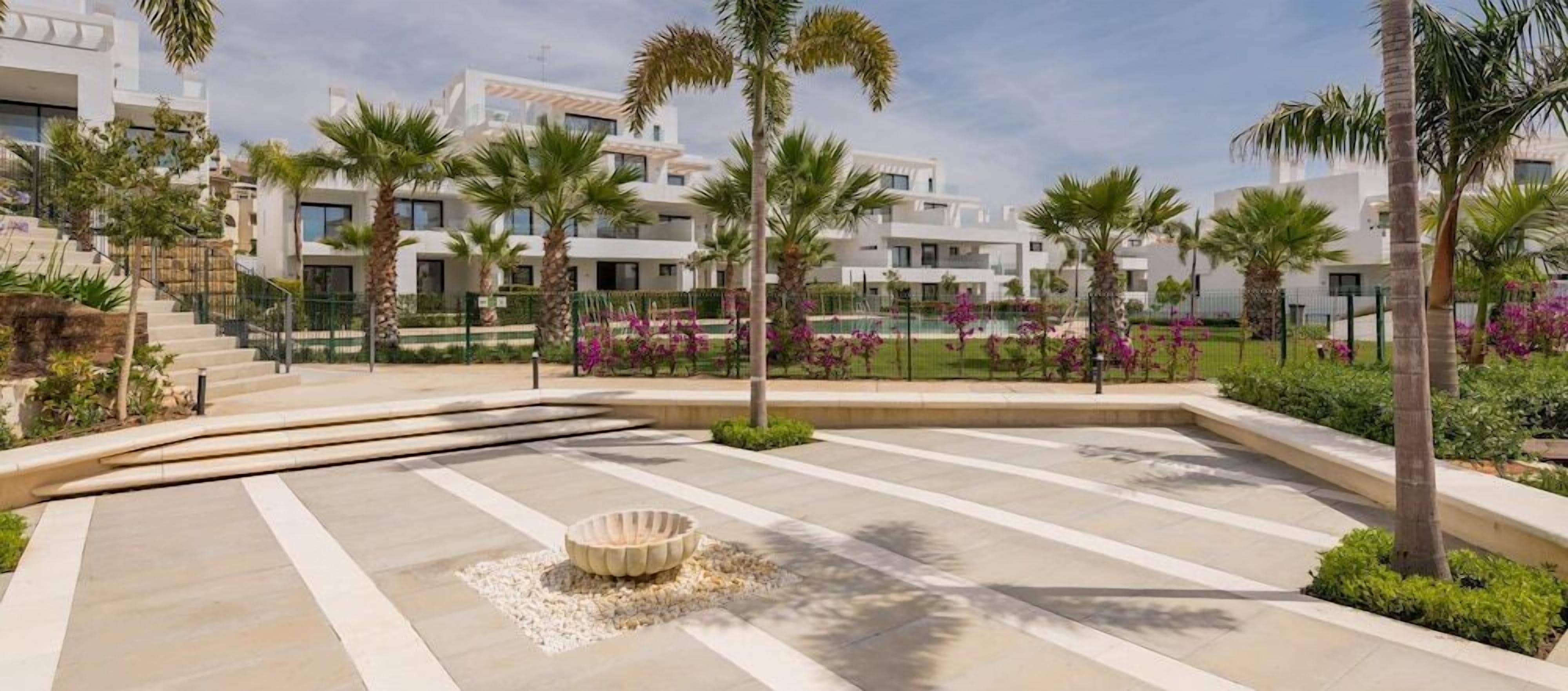 A modern resort with a pool area, palm trees, and a stone basin.